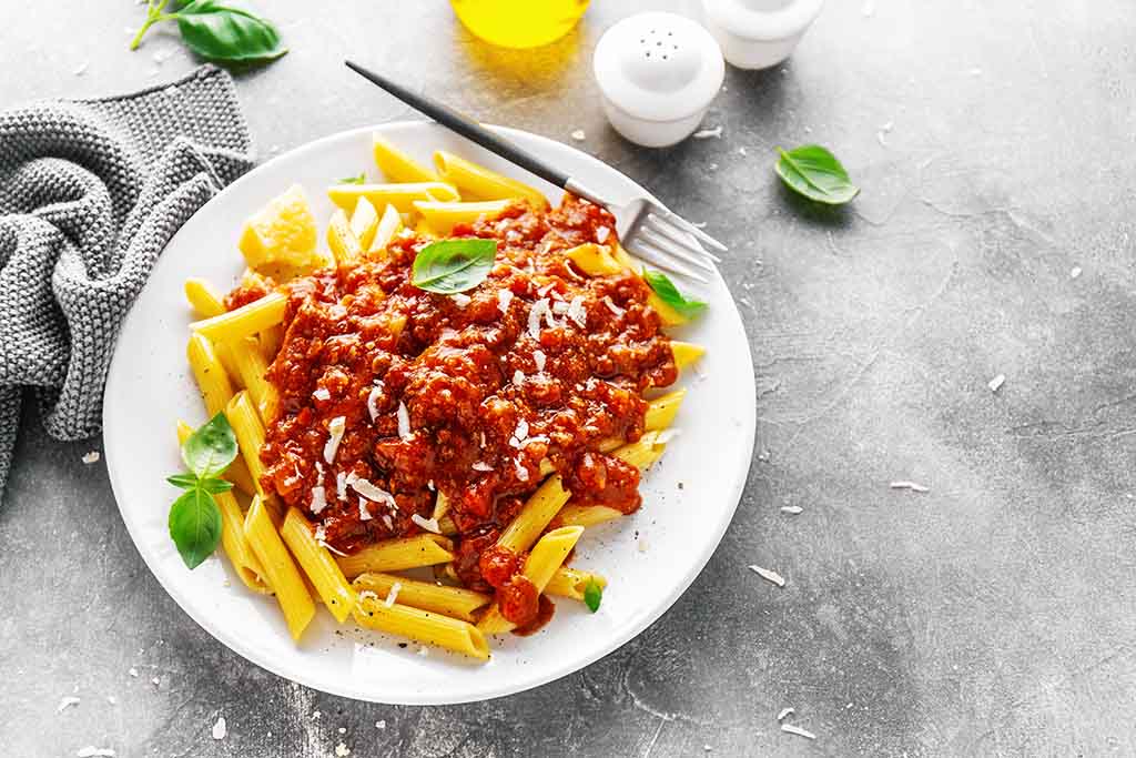 Tasty appetizing bolognese pasta penne with sauce and parmesan. Served on plate on grey background.  Closeup.